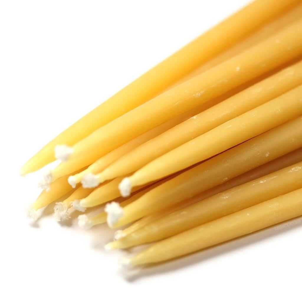 A close-up image features several Beeswax Birthday Candles from Gneiss Spice, highlighting their natural yellow color and rustic texture. These tapered candles, with visible wicks at one end, possess an earthy charm ideal for any setting.