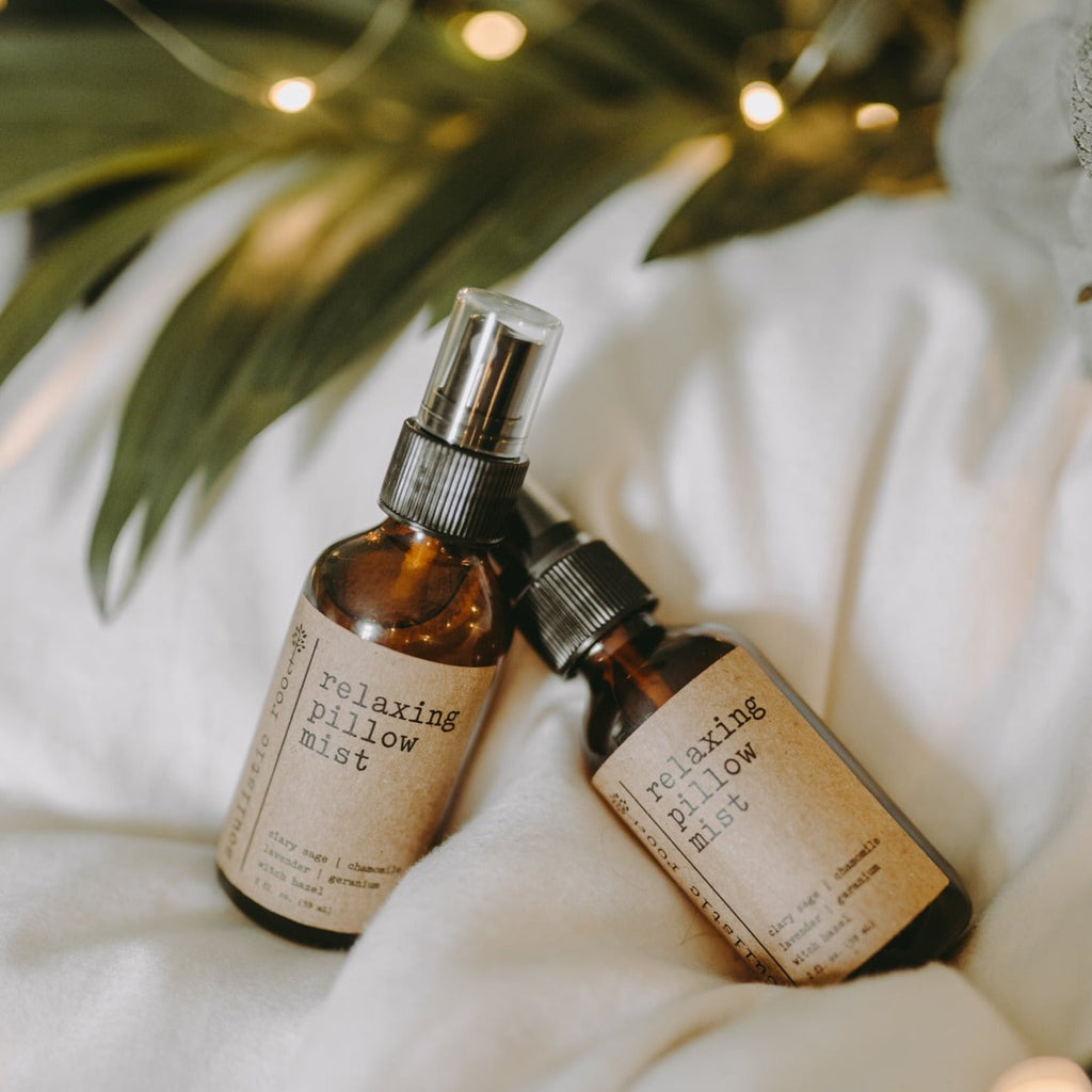 Relaxing essential oil pillow sprays on a white blanket next to a tree with lights.