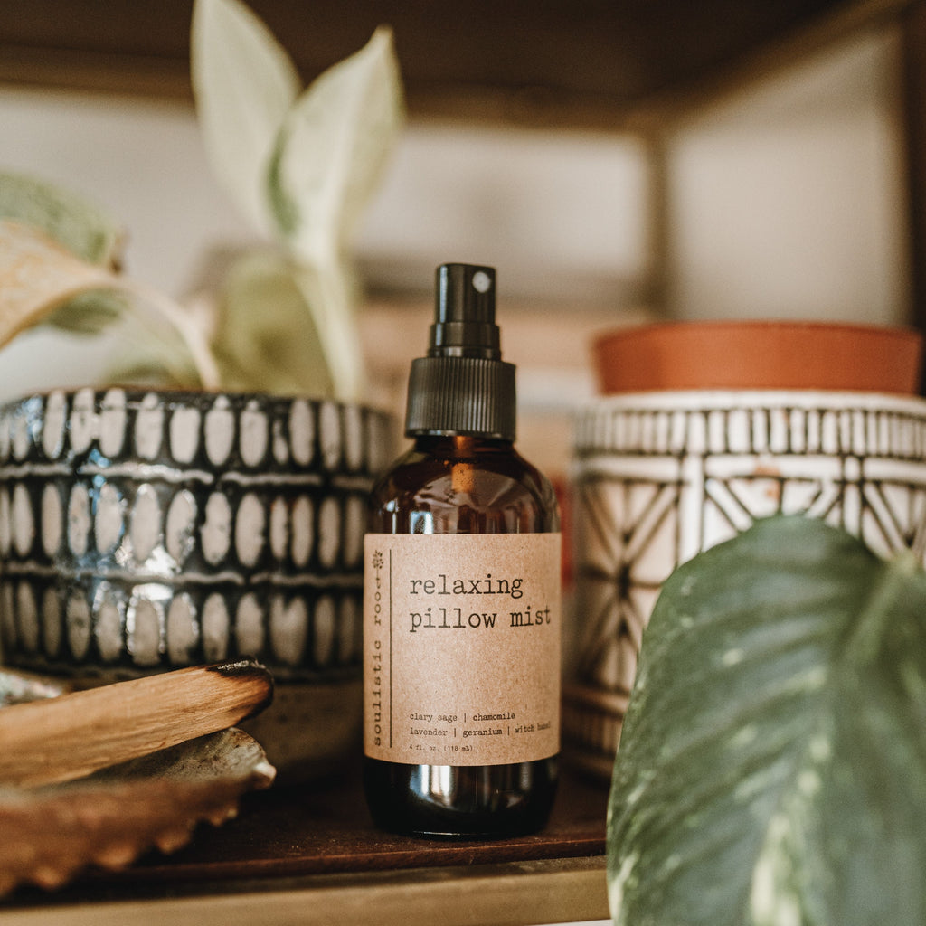 Relaxing pillow mist in a 4 oz amber glass bottle on a shelf next to decorative plants and a palo santo burning.